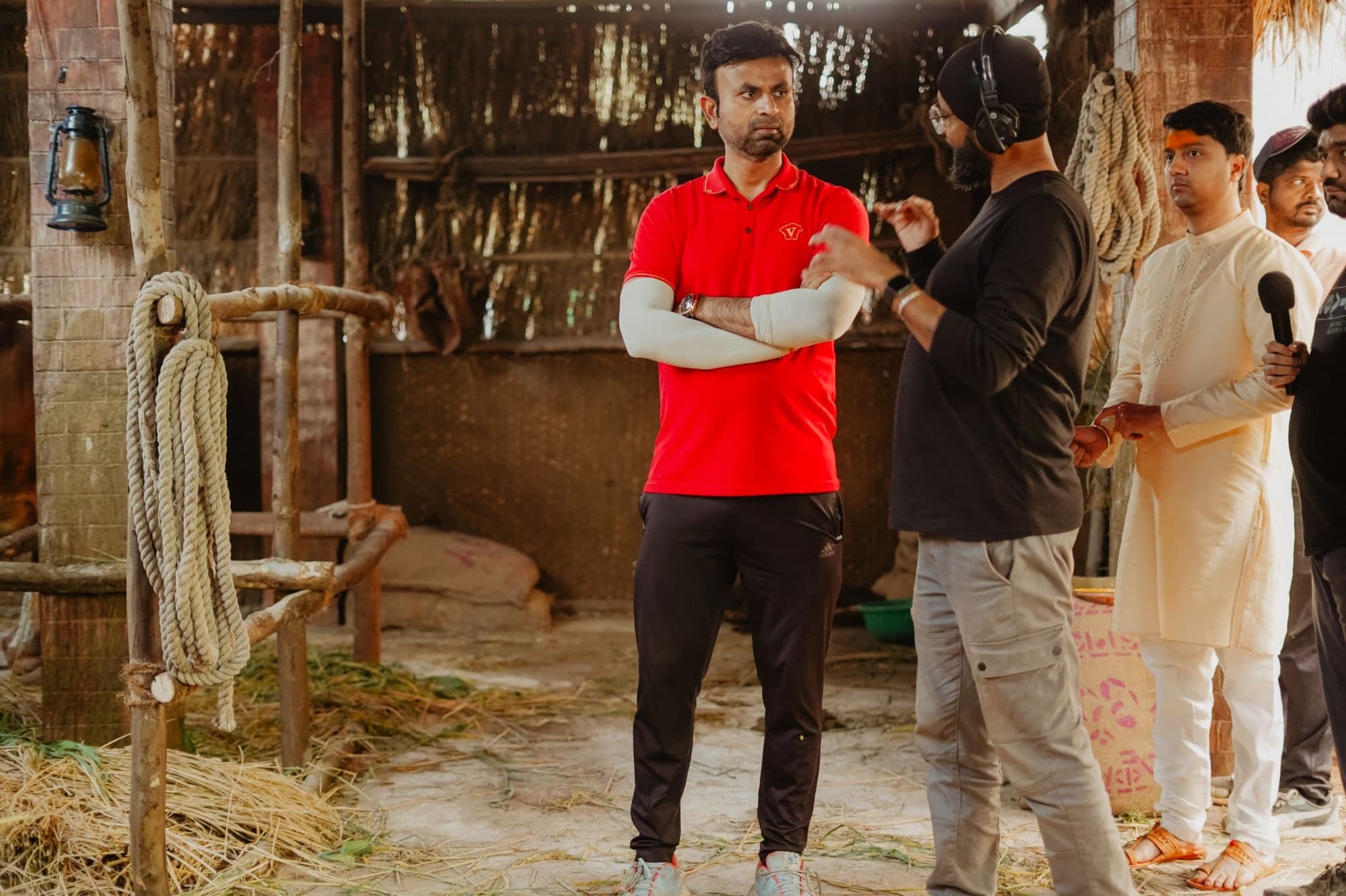Santosh Davakhar stands with his arms crossed in discussion with a crew member wearing headphones on the barn set, as other crew members look on behind them.