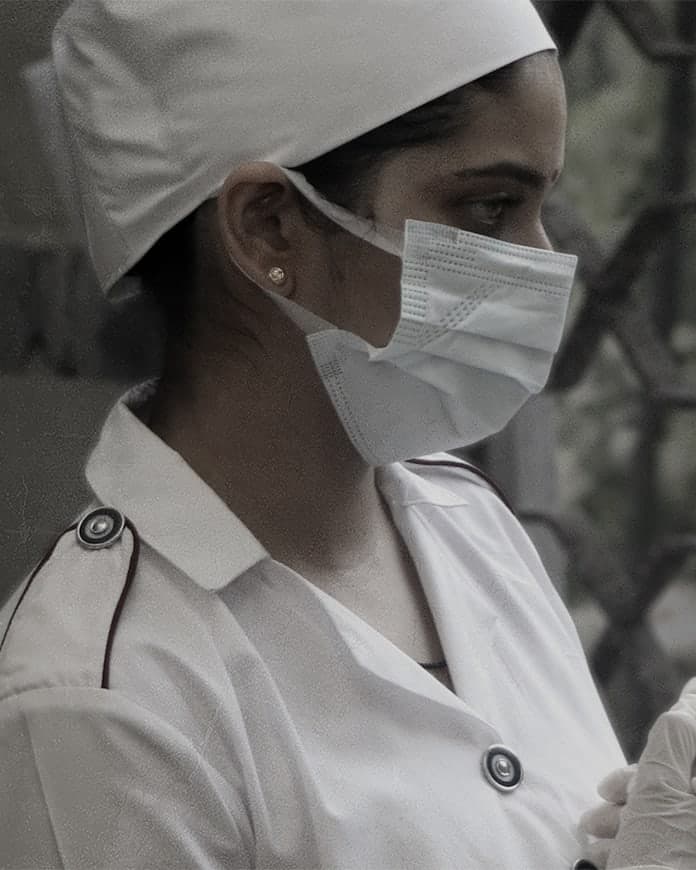 Antar-19 key art: a nurse in a white cap, surgical mask and gloves stands with her hands clasped beside an iron gate. Text: the title Antar-19 (अंतर-19); Based on true events; Written & directed by Santosh Davakhar; Produced by Diksha Santosh Davakhar; Deepti Lele, Kishor Chaughule; and the film’s credits.